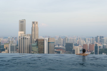 Young woman in a roof top swimming pool with beautiful Singapore city view. Vacation in Singapore