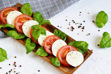 Mozzarella cheese with red tomatoes and basil leaves, pepper, olive oil, wooden desk, healthy food concept, white background