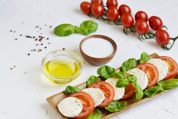 Mozzarella cheese with red tomatoes and basil leaves, pepper, olive oil, wooden desk, healthy food concept, white background