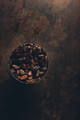 Obraz na płótnie Canvas top view of delicious cocoa beans in vintage bowl on dark rustic surface
