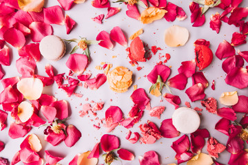 Very nice beautiful and vivid flat lay of pink and peach coloured  rose petals and french macarons dessert (crushed and whole ones) on the pastel purple background, top view