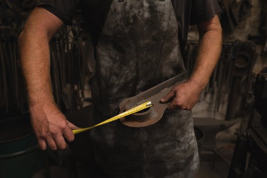 Blacksmith measuring a metal with measuring tape