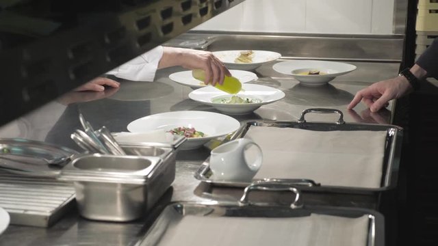Transit zone between kitchen and hall, prepared dishes are laid out for take them out. Hands of waiters put white plates on trays for giving to clients of cafe or restaurant. Side view. High Angle