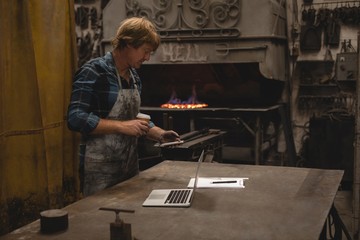 Blacksmith having coffee while using mobile phone