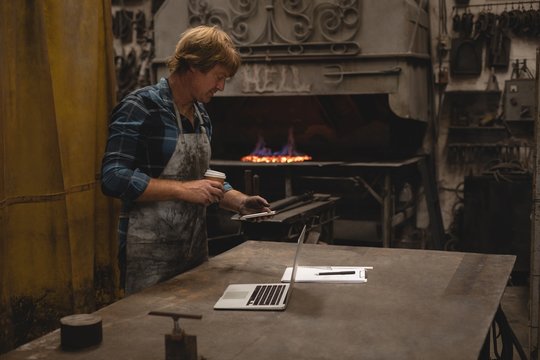 Blacksmith having coffee while using mobile phone