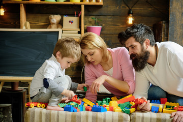 Father, mother and cute son play with constructor bricks. Kid with parents play with plastic blocks, build construction. Family on busy face spend time together in playroom. Caring parents concept.