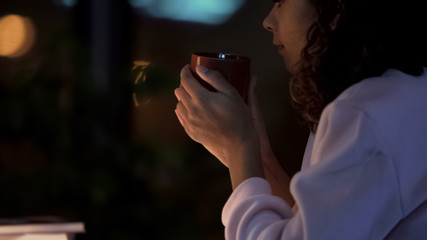 Young curly-haired woman drinking tea at restaurant, waiting for boyfriend