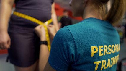 Personal trainer measuring waist of obese woman, checking results of exercising