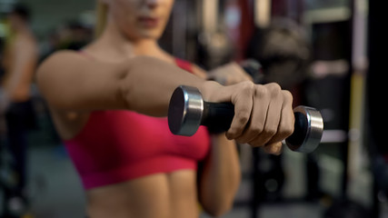 Fit woman doing dumbbell exercises, training in gym for strength and health