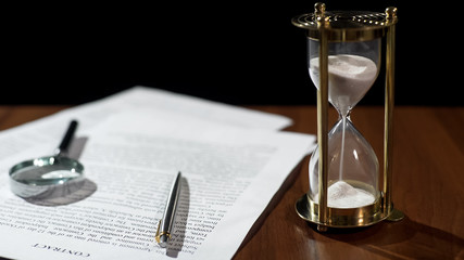 Close-up of document and hourglass on table, contract validity period expiring