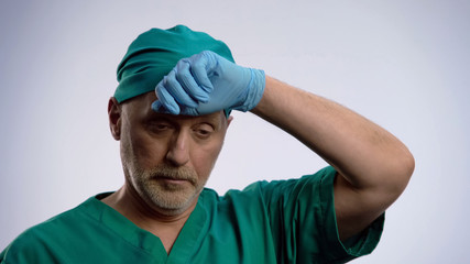 Tired male doctor wiping forehead after surgery, complex unsuccessful procedure