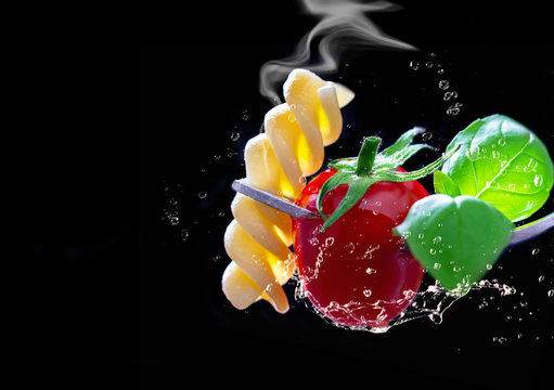 Pasta, tomato and basil on a fork, isolated against a black background