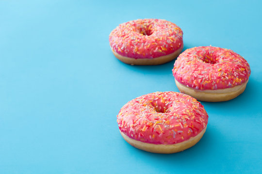 Pink frosted donut with colorful sprinkles on blue background. Copyspace