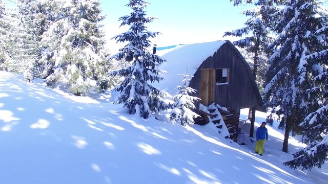 Adventurera woman rises up the wooden staircase to the attic of an old wooden hut in the mountains, among the huge snow-covered pine trees,. Sunny evening in the mountains.