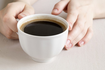 Hands holding a Cup of coffee on a bright table.