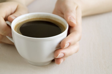 Hands holding a Cup of coffee on a bright table.