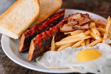 Breakfast plate on wood background. Grilled sausages, bacon, fried egg, fries potatoes