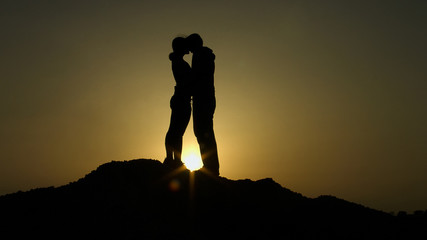 Fototapeta premium Silhouette of young couple in love hugging, kissing in sunset rays on mountain