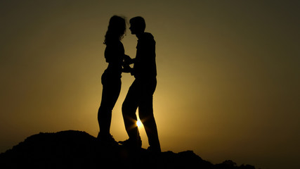 Man holding girl hands and trying to kiss her, romantic moment on hill at sunset