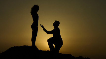 Fototapeta na wymiar Man making proposal to woman at dawn in mountains, happy couple in love engaging