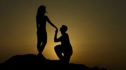 Silhouette of young man proposing to girlfriend on his knee, romantic engagement