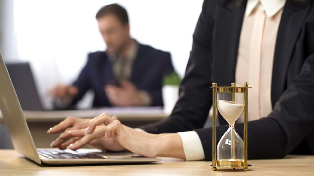 Businesswoman working on computer, hourglass trickling, outcome anticipation