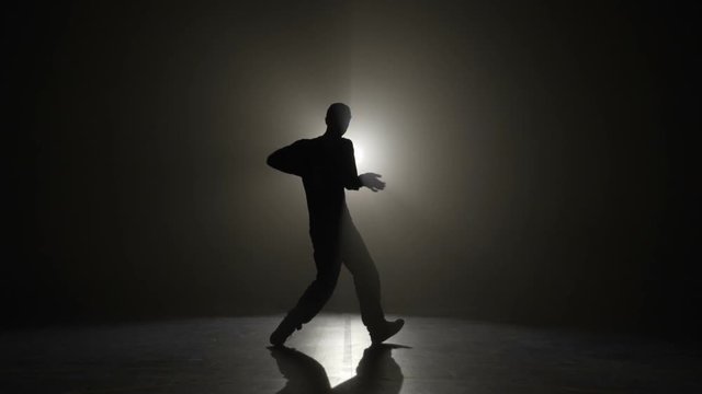 Slow motion silhouette of a man wearing cap and performing electric dance wave moves on a dark stage before the concert