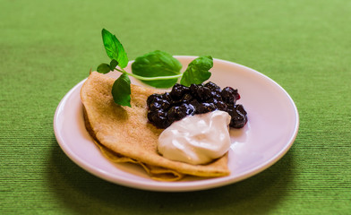 Portion of folded pancakes on a plate with jam and sour cream