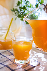 Juicy orange juice in a glass and jug and ripe fruit orange on a white table near the window, the concept of breakfast on a sunny summer day