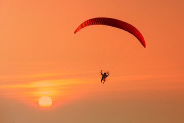 Naklejka na ściany i meble Silhouette of paraglider flying in the evening sky with sunset.
