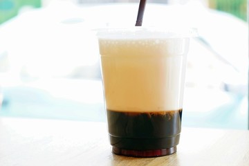 A iced two layers beverage consist of black coffee and milk in plastic cup with blurry bokeh background and copy space. A special iced coffee menu served with coffee jelly