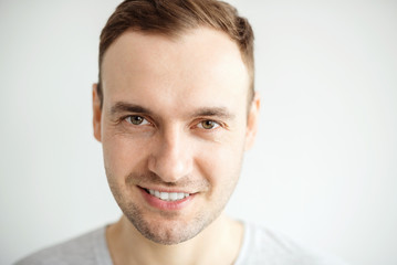 Naklejka premium Handsome young man with a bristle smiling teeth. Portrait of a guy in a gray shirt on a light background.