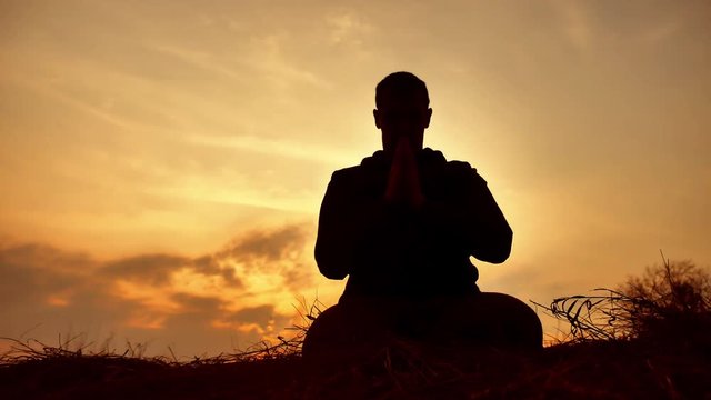 silhouette of a male monk engaged in meditation at sunset lifestyle sunlight. Buddhist prays at sunset healthy way of life nature