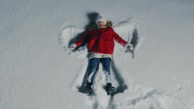 Top Down Footage of the Happy Cute Little Girl Falling into Snow, Lying and Making Snow Angel. Child Enjoying Winter Weather.