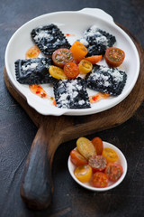 White plate with black ravioli on a rustic wooden serving board, vertical shot, selective focus