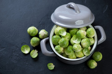 Pot with raw brussels sprouts over black stone background, elevated view with space, horizontal shot