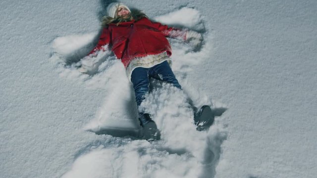 Top Down Footage of the Happy Cute Little Girl Falling into Snow, Lying and Making Snow Angel. Child Enjoying Winter Weather. Shot in Slow Motion.