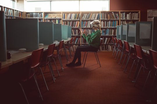 Side view of young woman looking through virtual reality headset while sitting in library