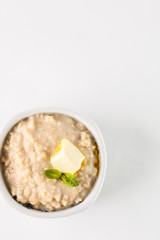 breakfast: oatmeal porridge with butter in white bowl on white background. Top view. Isolated