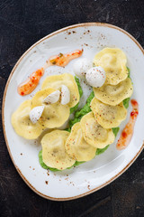 Italian ravioli with green peas puree, mozzarella and sauce on a plate, view from above, studio shot