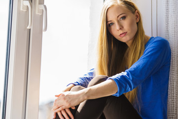 Sad depressed teen girl sitting on window sill