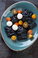 Turquoise plate with black ravioli, cherry tomatoes and mozzarella, view from above, vertical shot