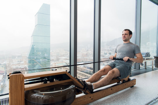 Man working out on row machine in fitness studio at scyscraper luxury hotel gym