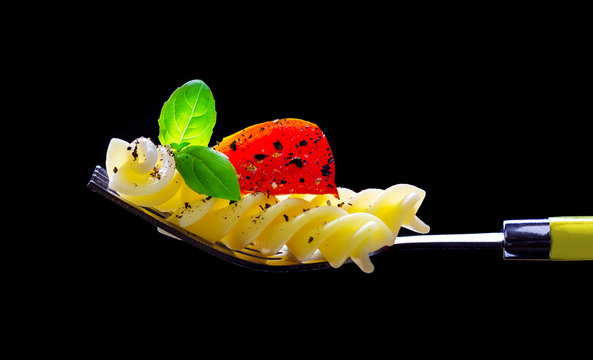 Pasta, tomato and basil on a fork, isolated against a black background