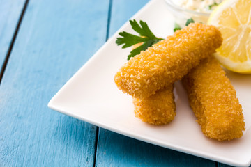 crispy fried fish fingers with lemon and sauce on blue wooden background