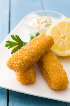 crispy fried fish fingers with lemon and sauce on blue wooden background
