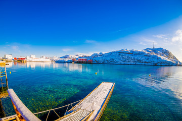 Outdoor view of amazing nature landscape with turquoise water and sunny day in blue sky with a floating structure in the lake and huge mountain covered with snow in Svolvaer