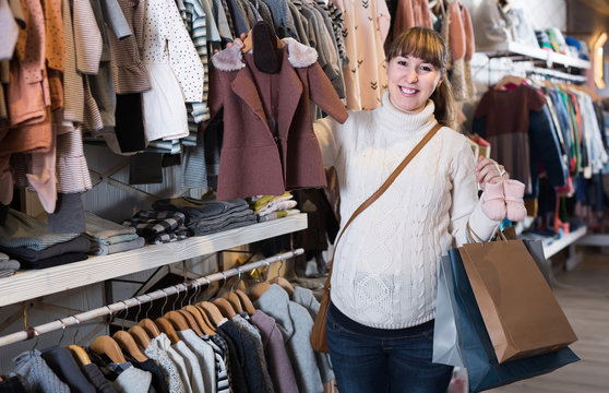 Pregnant woman showing her purchases in children’s clothes shop