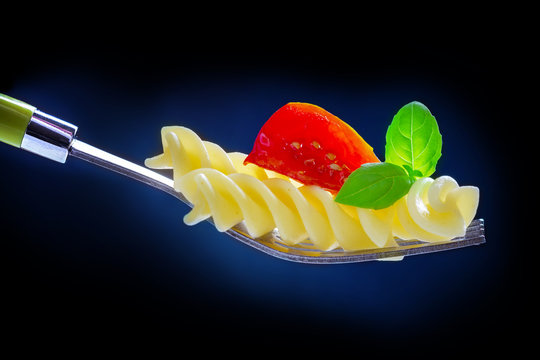 Pasta, tomato and basil on a fork, isolated against a blue - black background 