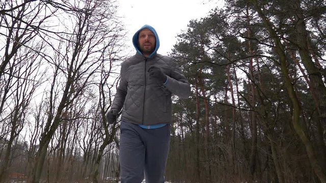Young happy man jogging in winter forest, super slow motion
